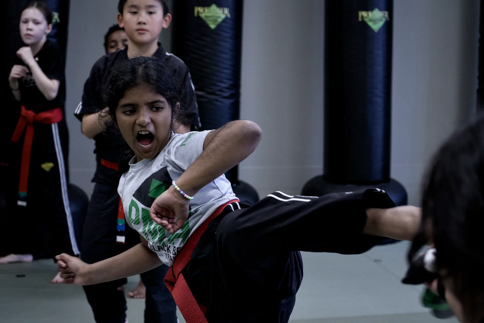 A girl in a red belt throwing a kick, shouting with effort