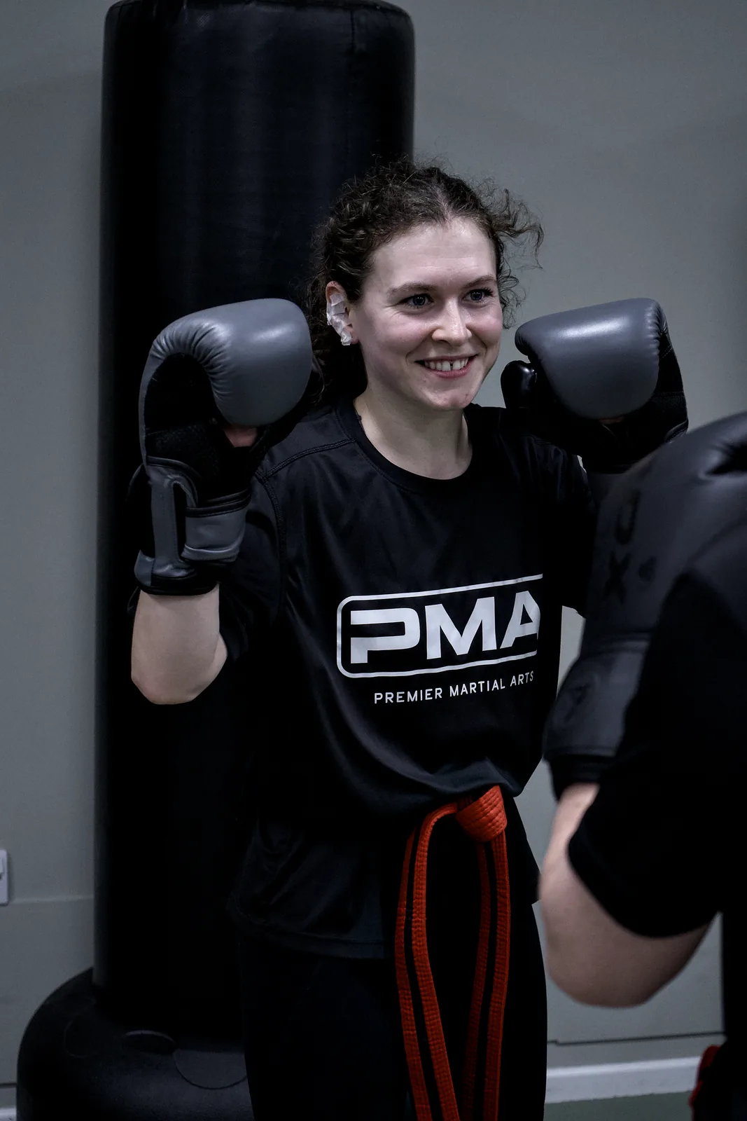 An adult student in boxing gloves smiling beside a punch bag