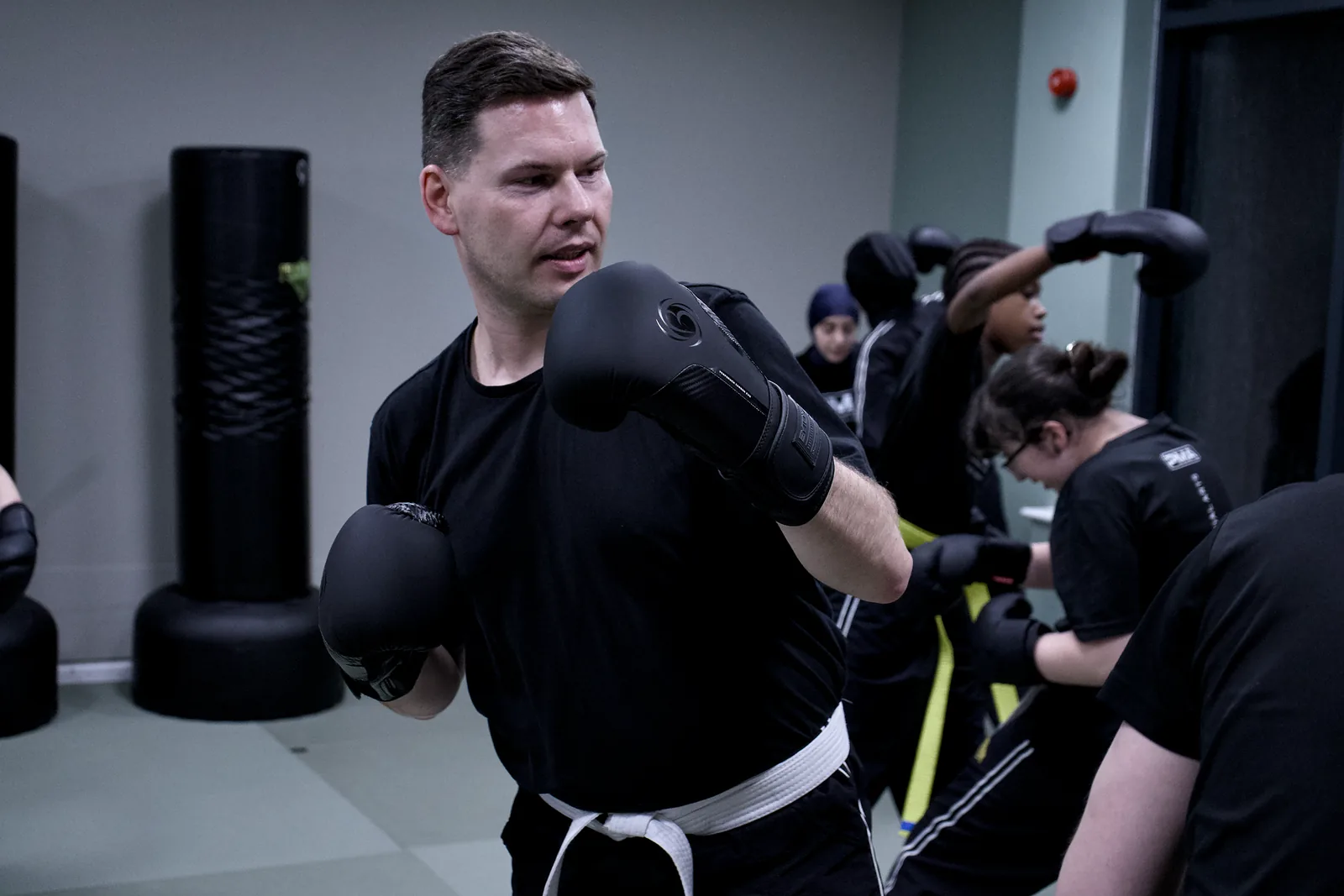 An adult in boxing gloves holding his guard while the class works behind him